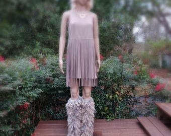 May include: A sleeveless light mauve dress featuring a drop-waist design with long, vertical fringe detailing from the waist down. The dress is paired with textured, shaggy, multi-tonal gray and brown faux fur leg warmers.