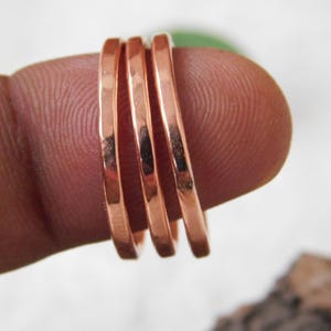 Könnte beinhalten: Vier dünne, kupferfarbene Ringe, die auf einem Finger gestapelt sind. Die Ringe haben eine glatte, polierte Oberfläche und einen warmen, rötlich-braunen Farbton. Die Ringe sind schlicht und elegant, für den Alltag geeignet.