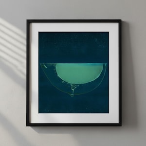 May include: Abstract art print in a black frame. The artwork features a semi-circular shape with a light green interior against a dark blue background. A single drop of liquid is visible at the bottom.