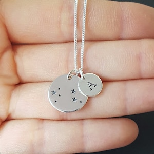 May include: Silver necklace with two charms. One charm is a circle with a constellation of stars and the other charm is a circle with the letter A.