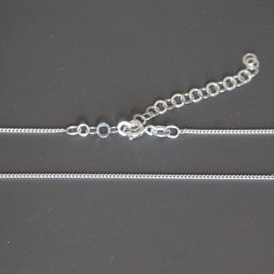 May include: A silver chain necklace with a lobster clasp closure. The chain is made of small, round links.