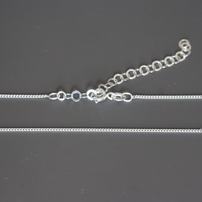 May include: A silver chain necklace with a lobster clasp closure. The chain is made of small, round links.