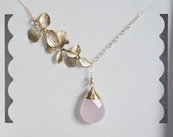May include: A gold necklace with a delicate chain and a pendant featuring three gold orchid flowers and a pink gemstone drop.