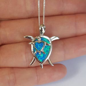 May include: A silver necklace with a blue opal turtle pendant. The turtle is holding a smaller turtle in its shell, and the opal is a heart shape.