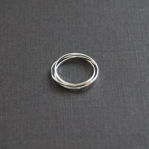 May include: Three silver rings interlocked together, forming a circle. The rings are smooth and shiny, and they are set against a dark gray background.