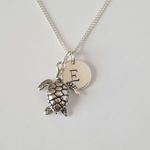 May include: Silver necklace with a turtle charm and a round disc charm with the letter "E" engraved on it.
