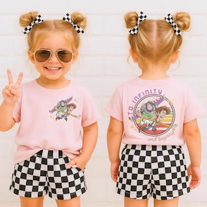 May include: A young child wearing a light pink t-shirt and black and white checkered shorts. The t-shirt features a graphic of Buzz Lightyear and Woody from Toy Story. The text "To Infinity and Beyond" is on the back of the shirt.