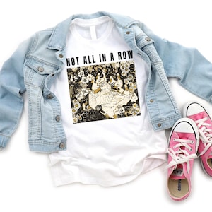 May include: White t-shirt with the text "NOT ALL IN A ROW" above a graphic of ducks and flowers. A light blue denim jacket and pink sneakers with white laces are also in the image.