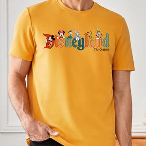 Pu&ograve; includere: T-shirt girocollo giallo senape con il logo Disneyland, con Topolino, Minnie, Paperino, Paperina, Pippo e Pluto. Il testo "The Original" &egrave; sotto il logo. La maglietta &egrave; di colore unito.