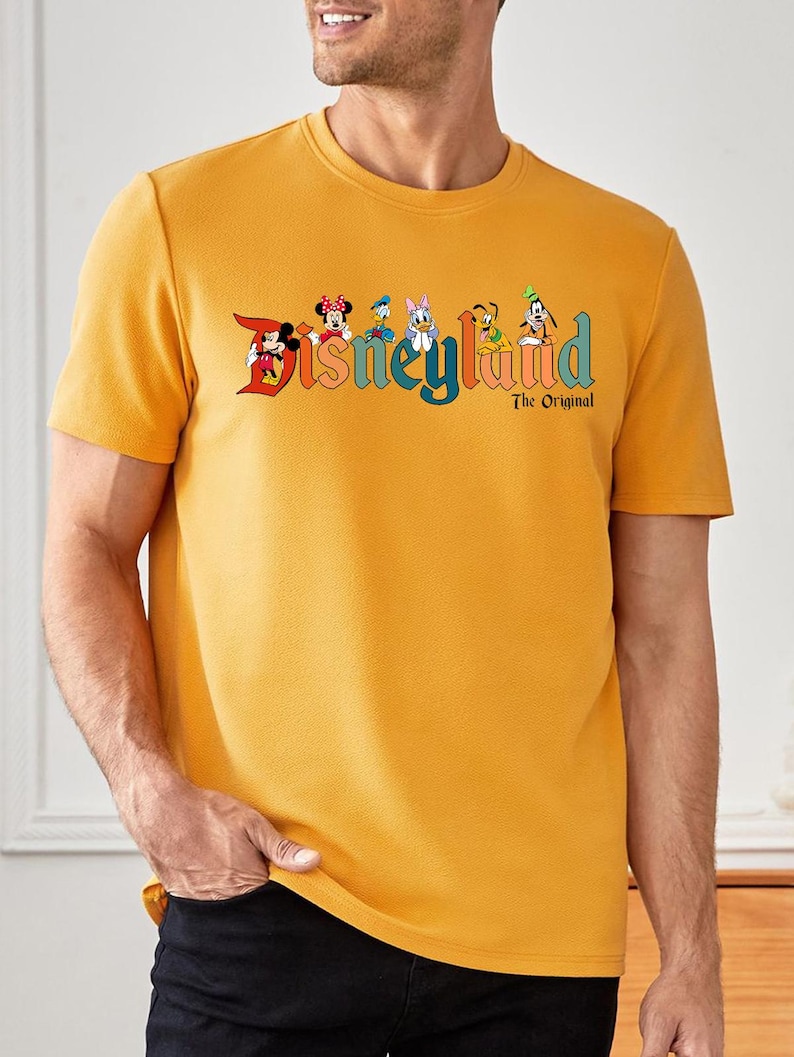 Pu&ograve; includere: T-shirt girocollo giallo senape con il logo Disneyland, con Topolino, Minnie, Paperino, Paperina, Pippo e Pluto. Il testo "The Original" &egrave; sotto il logo. La maglietta &egrave; di colore unito.