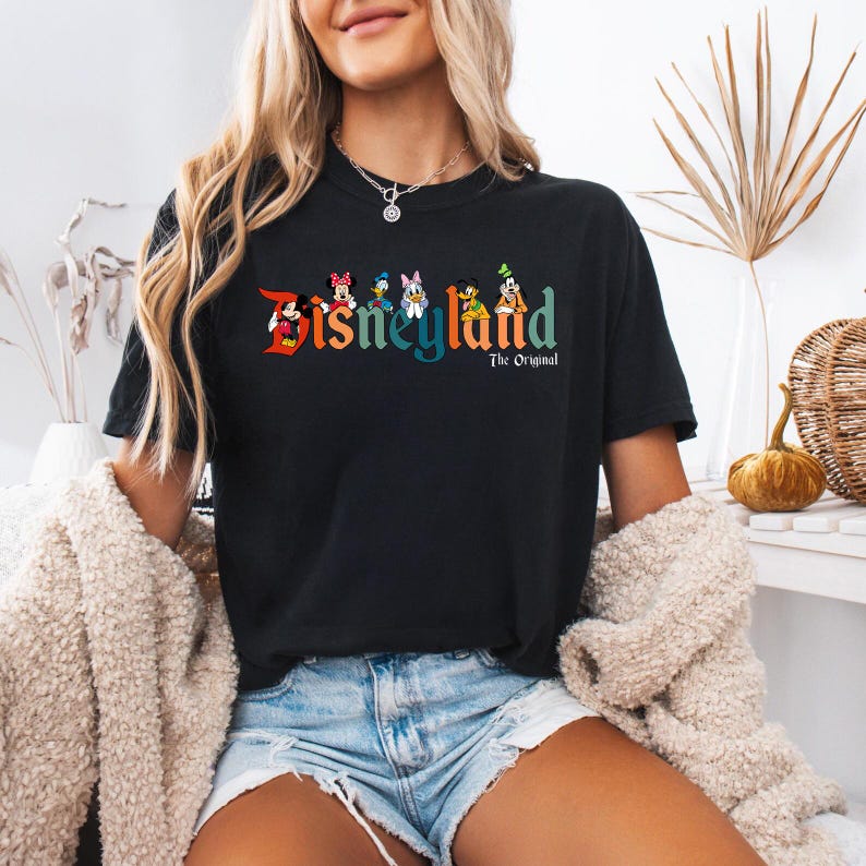 Pu&ograve; includere: T-shirt nero con la scritta "Disneyland" in lettere colorate e personaggi dei cartoni animati. Il testo "The Original" &egrave; sotto la parola Disneyland. La maglietta &egrave; a girocollo.