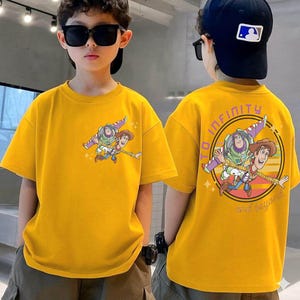 May include: Yellow t-shirt featuring a cartoon graphic of Buzz Lightyear and Woody. The front of the shirt shows the characters flying, while the back has a circular design with the words "TO INFINITY AND BEYOND".