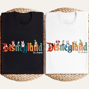 Pu&ograve; includere: T-shirt nere e bianche con grafica Disneyland. La grafica presenta la parola "Disneyland" in lettere colorate con personaggi Disney. Il testo "The Original" &egrave; sotto la parola Disneyland.