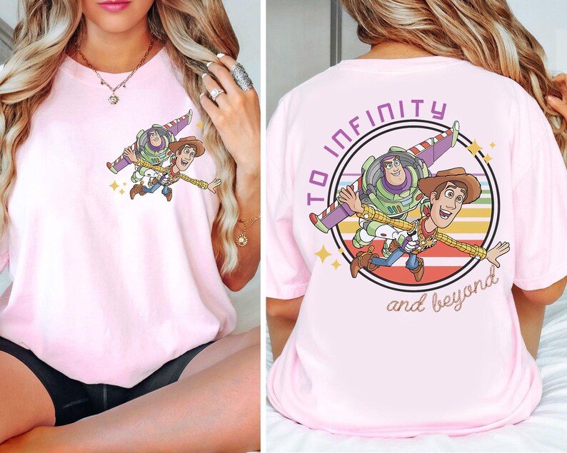 May include: A light pink t-shirt featuring a graphic of Buzz Lightyear and Woody from Toy Story. The front of the shirt shows the characters flying. The back of the shirt has the phrase "To infinity and beyond" in a circle.