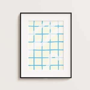 以下が含まれることがあります： グリッドパターンが特徴の額入りアートプリント。アートワークは、薄い黄色の背景に青いグリッドが重ねられています。フレームは黒で、プリントは白い壁に表示されています。