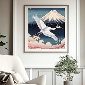 以下が含まれることがあります： 日本のスタイルのイラストが描かれた、額装されたアートプリント。白い鶴が雪をかぶった山の前を飛び、青い空とピンクの雲を背景にしています。アートワークは白いフレームに展示されています。