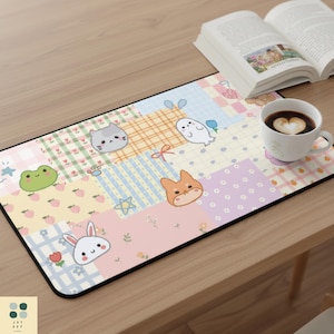 May include: A rectangular desk mat with a patchwork design featuring cartoon animals and pastel colors. The mat includes a cat, fox, frog, ghost, and bunny. A cup of coffee and an open book are on the wooden table.