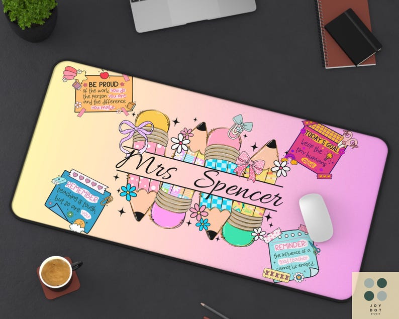 May include: A personalized desk mat with a gradient yellow to pink background. The mat features pencil illustrations, floral accents, and the name "Mrs Spencer" in a script font. Inspirational quotes are also included.