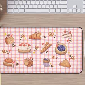 Op de afbeelding: Een rechthoekige muismat met een speelse illustratie van gebak, waaronder croissants en cakes, tegen een roze en paars geruit patroon. Het ontwerp bevat harten en hagelslag.