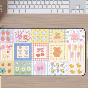 Peut inclure: Tapis de souris rectangulaire avec un motif patchwork coloré. Le motif comprend des fraises, des lapins, des ours, des nœuds, des cerises, un gâteau, des cornets de glace, des fleurs et des canards. Le tapis de souris est sur un bureau en bois avec un clavier et une souris.