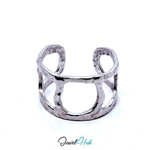 May include: A silver cuff bracelet with a textured, hammered finish. The open design features three rounded cutouts. The jewellery is set against a white background.