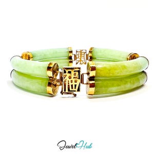 Op de afbeelding: Een lichtgroene jade armband met gouden details. De armband heeft twee parallelle jade banden die zijn verbonden door gouden sluitingen met Chinese karakters. Het Jewel Hub-logo staat onderaan.
