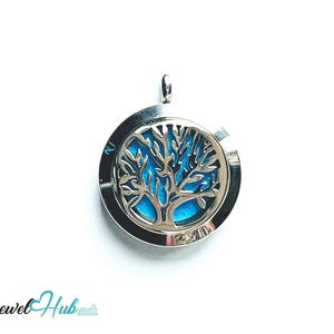 May include: A silver-colored pendant with a tree of life design. The pendant has a circular shape with a blue background. The tree design is in the center of the pendant. The pendant has a small loop at the top for a chain.