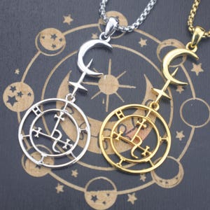 May include: Two pendant necklaces. One is silver-toned, the other gold-toned. Each features a crescent moon and cross design above a circular pendant with symbols. The necklaces are displayed on a dark background with celestial patterns.