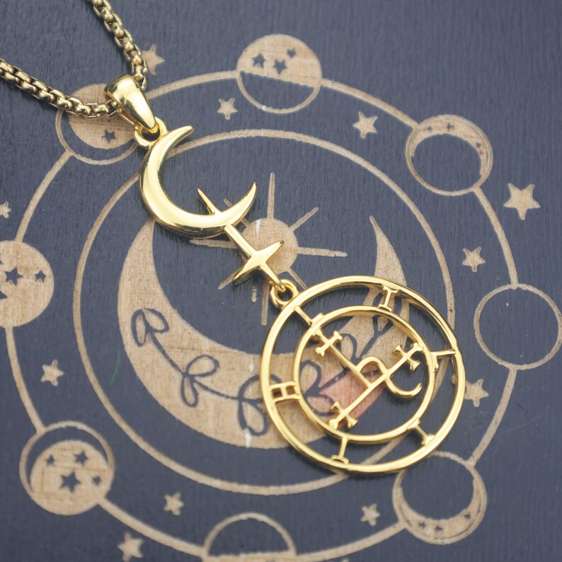 May include: Gold-colored pendant necklace featuring a crescent moon, star, and circular design with intricate symbols. The necklace hangs on a gold chain against a dark blue background with celestial patterns. A unique piece of jewelry.