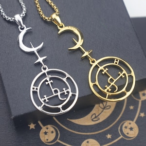 May include: Two pendant necklaces. One is silver-toned, the other gold-toned. Each features a crescent moon, a cross-shaped element, and a circular pendant with an intricate design. The gold necklace has the letter "H" on it.