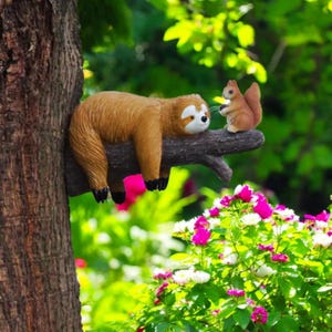 May include: A brown sloth ornament and a squirrel ornament perched on a tree branch. The sloth has a white face and black feet. The squirrel is holding a nut. The background features green foliage and colourful flowers.