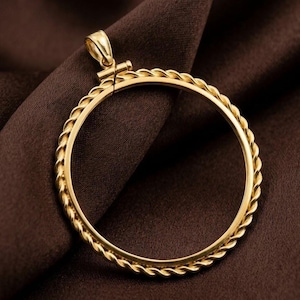 May include: A gold-colored pendant with a circular design. The pendant has a braided rope-like texture around the outer edge of the circle. The pendant is on a brown fabric background.