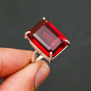 Peut inclure: Une bague en argent ornée d'une grande pierre précieuse rectangulaire rouge foncé. La pierre est facettée, captant la lumière et affichant une couleur riche et vibrante. Le sertissage de la bague est simple.