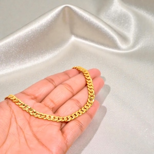 May include: A gold-colored chain necklace featuring a classic curb link design. The chain is composed of interlocking, flattened oval links that create a uniform, continuous pattern. The metal has a bright, reflective finish that catches light.