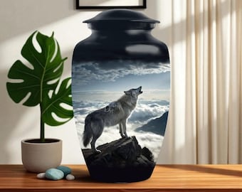 Könnte beinhalten: Schwarze Urne mit einem heulenden Wolf auf einer Berglandschaft. Die Urne hat eine glänzende Oberfläche und einen abnehmbaren Deckel. Der Wolf ist grau und weiß, vor einem bewölkten Himmel. Ein dekorativer Artikel zur Erinnerung an einen geliebten Menschen.