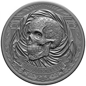 May include: A silver coin featuring a detailed sugar skull design, adorned with floral patterns. The skull is set against a draped background, with the words "Día de los Muertos" inscribed on a banner. The coin's edge has a textured pattern.