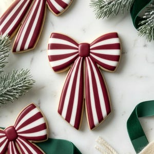 Könnte beinhalten: Draufsicht auf schleifenförmige Kekse mit rot-weißen Streifen, angeordnet mit Tannenzweigen und einem grünen Band auf einer Marmoroberfläche. Die Kekse haben einen hellbraunen Rand.