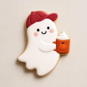 May include: A Halloween cookie in the shape of a ghost wearing a maroon baseball cap. The ghost holds an orange mug with a pumpkin design and whipped cream. The cookie has a white base with a brown outline.