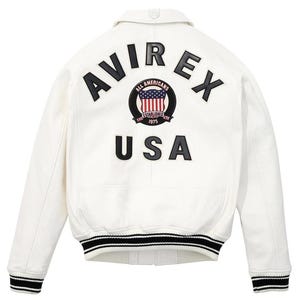 K&ouml;nnte beinhalten: Wei&szlig;e Lederjacke mit schwarz-wei&szlig; gestreiften B&uuml;ndchen und Saum. Auf der R&uuml;ckseite steht "AVIREX" &uuml;ber einem kreisf&ouml;rmigen Emblem mit US-Flaggen-Design und dem Text "ALL AMERICANS ESTABLISHED 1975". Darunter steht das Wort "USA".