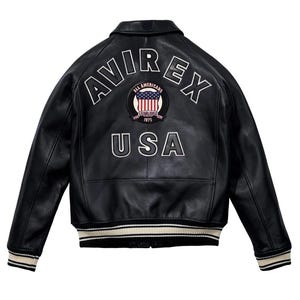 K&ouml;nnte beinhalten: Schwarze Lederjacke mit wei&szlig;er gestickter Schrift "AVIREX" und "USA". Mit einem Aufn&auml;her mit der amerikanischen Flagge und dem Text "ALL AMERICANS ESTABLISHED 1975". Die Jacke hat einen gerippten Kragen, Manschetten und Saum mit cremefarbenen und schwarzen Streifen.