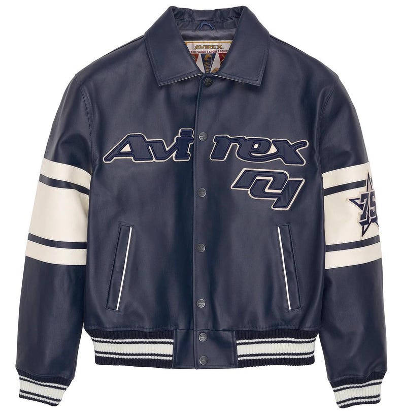 K&ouml;nnte beinhalten: Marineblaue Lederjacke mit wei&szlig;en Akzenten und dem Text "Avirex 74". Die Jacke hat einen Kragen, Druckkn&ouml;pfe und gestreifte B&uuml;ndchen und Saum. Wei&szlig;e Streifen verlaufen die &Auml;rmel hinunter.