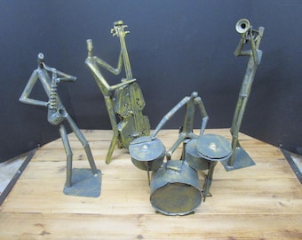 Könnte beinhalten: Ein Set aus vier Metallskulpturen, die eine Jazzband darstellen, bestehend aus einem Saxophonisten, einem Kontrabassisten, einem Schlagzeuger mit Schlagzeug und einem Trompeter. Jede Figur ist aus dunklem, verwittertem Metall mit Goldtönen gefertigt.