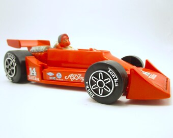Könnte beinhalten: Ein orangefarbenes Tonka-Spielzeug-Rennauto mit der Nummer 14, dem Namen A.J. Foyt und einer Fahrerfigur mit rotem Helm. Das Fahrzeug hat schwarze Räder mit weißem Tonka-Schriftzug, einen Heckspoiler und sichtbare Motordetails hinter dem Cockpit.