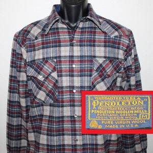 May include: A blue and white checked flannel shirt with a red and green checked pattern. The shirt has a label that reads "WARRANTED TO BE A PENDLETON TRADE MARK REG. U.S. PAT. OFF. PENDLETON WOOLEN MILLS PORTLAND, OREGON 100% VIRGIN WOOL M PURE VIRGIN WOOL MADE IN U.S.A."
