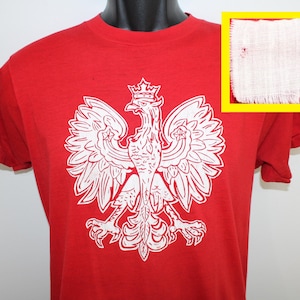 May include: Red t-shirt featuring a white graphic of the Polish national emblem, a white eagle with a crown on its head.