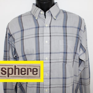 May include: A light gray button-down shirt with a plaid pattern in shades of blue and black. The shirt has a chest pocket and a button-down collar. The word "sphere" is displayed on a yellow rectangle.