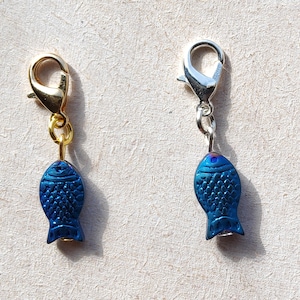 May include: Two blue fish charms with gold and silver lobster clasps. The fish charms have a textured surface and are iridescent.