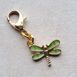 May include: A gold-coloured charm featuring a green dragonfly design. The charm has a lobster claw clasp.