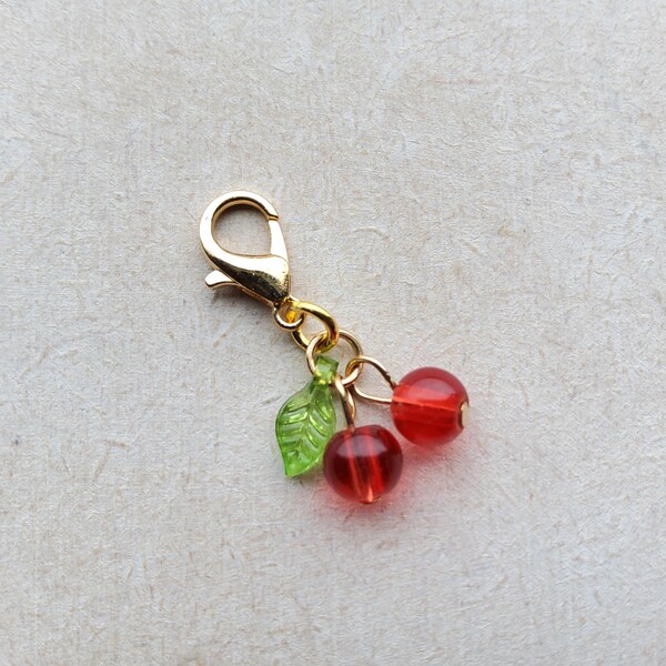 Charm de cereza roja con cierre de clip, cierre de langosta dorado, marcador de puntada, cremallera y planificador.