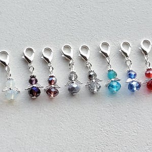 Pode incluir: Uma coleção de onze pingentes de anjo com fechos prateados. Cada pingente apresenta uma pequena figura de anjo com asas de cristal e um corpo de contas em várias cores, incluindo transparente, rosa, roxo, azul, vermelho e verde.